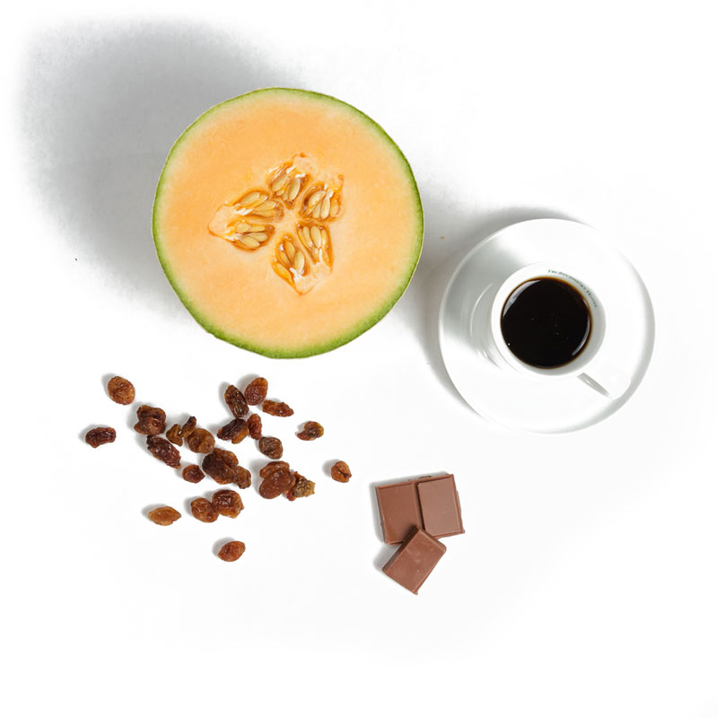 Pohár kávy vedľa žltého melónu, hrozienok a horkej čokolády